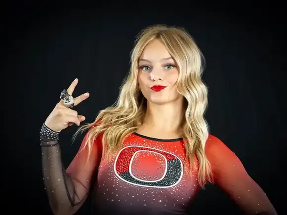 Dancer in red bedazzled costume with sheer sleeves making peace sign with two championship rings against black background - dance studio portrait photography Boise Meridian Nampa