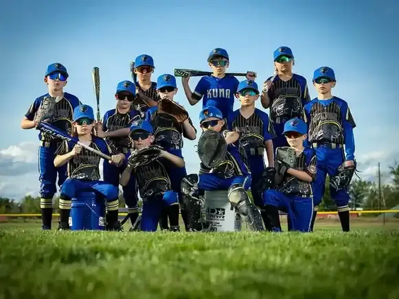 Kuna youth baseball team in blue and black uniforms posing with bats and gloves on grass field - professional team photography for leagues and travel teams
